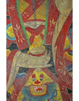 Close-up of Laotian parchment painting with stylized hands, bowl, and grinning blue-bearded face in double plexiglass.