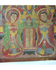 Brown Laotian parchment painting with two haloed figures beside a scroll, double plexiglass frame, close-up view.