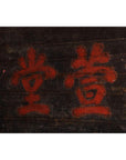 Close-up of a dark wooden 19th century Chinese signboard with red Chinese characters on a worn surface.