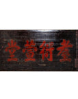 Close-up of a 19th century wooden signboard with large red Chinese characters and smaller text along the right edge.