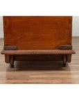 Close-up of brown teak wood blanket chest with iron nailheads on wheels, placed on a wood floor.