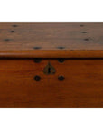 Close-up of a large brown teak wood blanket chest with iron nailheads, keyhole, and wheels.