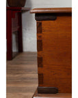 Close-up of brown teak wood blanket chest with iron nailheads and wheels, on a wooden floor.
