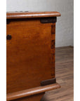 Close-up of a large brown teak wood blanket chest with iron nailheads on wheels, on wooden floor indoors.