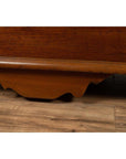 Close-up of brown carved teak wood base with iron nailheads and wheels from a large antique Javanese chest.