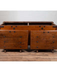Brown teak wood blanket chest with iron nailheads on wheels, placed on a wooden floor.