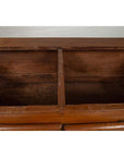 Brown teak wood blanket chest with iron nailheads on wheels, open to show two compartments.