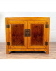 Two-toned burl and elm wood Chinese antique cabinet with doors against a white brick wall indoors.