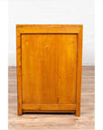 Two-toned burl and elm wood antique cabinet with doors, positioned against a light brick wall and wood floor indoors.