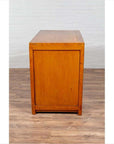 Two-toned burl and elm wood cabinet with doors, on a wooden floor next to a white brick wall.