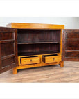Brown burl and elm wood patina cabinet with doors, shelf, and drawers against a white wall on wood floor indoors.