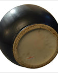 Black celadon ceramic vase upside down, showing textured unglazed base with sticker label, close-up view.