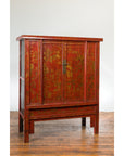 Red lacquered 19th century armoire with gilt décor on four legs, displayed on a wooden floor.