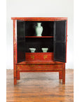 Red lacquer 19th c. armoire with gilt décor, green vase and two bowls on shelves above two drawers.