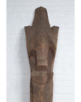 Brown wood Singa Singa Batak tribal face carving, hand carved, displayed against a white brick wall.
