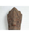Brown hand carved wooden Singa Singa tribal mask from Batak people of Sumatra, displayed against white brick wall.