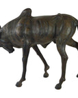 Brown leather wildebeest sculpture with head lowered and legs bent, placed on a plain surface.