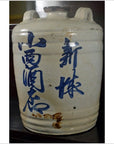 Close-up of a large ceramic sake jar from Japan, Meiji/Taisho period, with blue calligraphy and small spout on dark background.