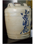 Blue and white ceramic sake jar with calligraphy and handles from Meiji/Taisho Japan on a dark surface.