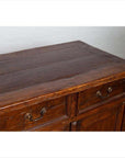 Close-up of brown teak wood cabinet with four drawers, double doors, and metal handles, indoors against a white wall.