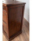 Close-up of a brown teak wood cabinet with four drawers and double doors on a wooden floor.