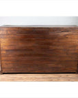 Brown teak wood cabinet with four drawers and double doors, placed on a wooden floor against a white brick wall indoors.