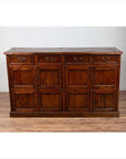 Brown teak wood cabinet with four drawers and four double doors, placed indoors against a white brick wall.