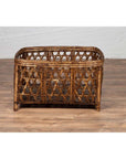 Brown bamboo fretwork basket with short feet, vintage Thai style, on wooden floor next to white brick wall.