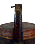 Close-up of a brown wicker basket with lid next to a string instrument neck, both shown against a plain background.