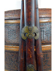 Brown carved wooden staffs with metal fittings resting against a large wicker basket with lid, indoor setting.