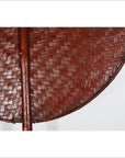 Close-up of a round brown woven fan with central handle, made from natural material, on a white background.