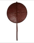 Brown woven fan with a round shape and long handle on a white background.