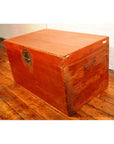 Brown leather coffee table trunk with metal handles on wooden floor beside a white brick wall.