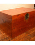 Brown leather coffee table trunk with metal handles and a round lock on a wooden floor by a white brick wall.