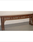Long bamboo altar table with geometric latticework, positioned against a white wall on a gray floor.