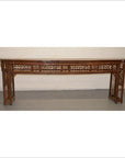 Brown bamboo altar table with intricate latticework and geometric patterns, positioned against a plain wall.