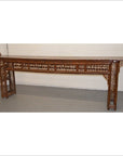 Brown bamboo altar table with intricate latticework and lacquer finish, positioned in front of a plain wall.