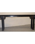 Long antique Chinese altar table with carved spandrels, dark wood, against a white wall and gray floor.