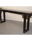 Dark wood antique Chinese altar table with carved spandrels, positioned against a plain white wall and grey floor.