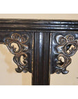 Close-up of dark wood antique Chinese altar table leg with intricate swirling carved spandrels.