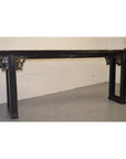 Black antique Chinese wood altar table with carved spandrels, positioned against a white wall and gray floor.