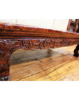 Close-up of a dark wood carved table with ornate floral designs and claw feet on a polished wooden floor.