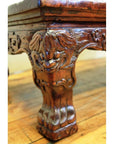 Brown carved wood table with floral and leaf motifs, claw feet, on polished hardwood floor.
