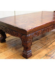 Brown wood low carved table with ornate carved legs and claw feet on a wooden floor.