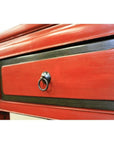Close-up of red lacquer wood side table drawer with black trim and black metal ring pull handle.