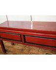 Red lacquer wood low side table with two black-trimmed rectangular panels on a wooden floor, light background.