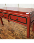 Red lacquer and black trim side table with two drawers on wood floor against a light-colored wall.