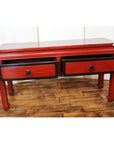 Red lacquer and black trim low side table with ring handles on a wooden floor.