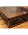 Brown wooden Kang coffee table with carved edges, gilt accents, and open shelf on hardwood floor.