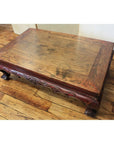 Square elmwood table with carved legs and ornate border on a hardwood floor, close-up view.